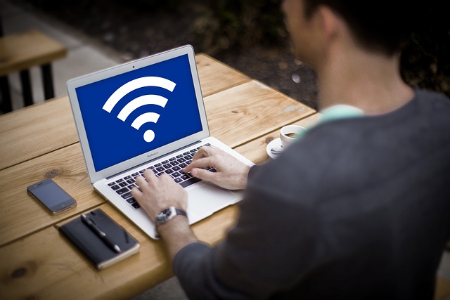 A man sitting at a desk with a laptop open and a WiFi symbol on the screen.